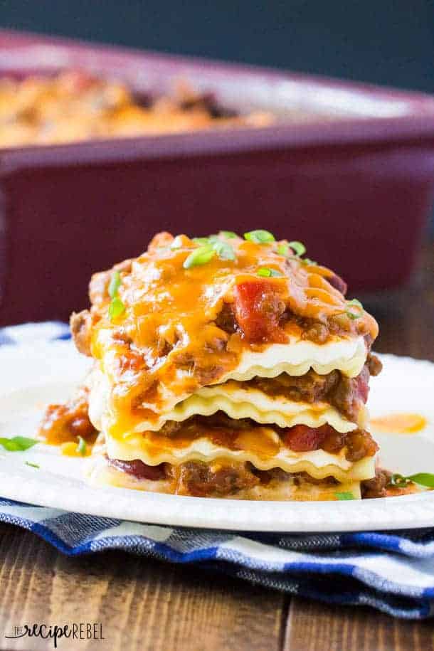 piece of bbq chili lasagna on white plate with pan of lasagna in the background