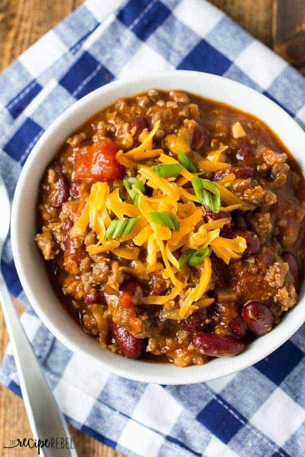 overhead image of white bowl filled with chili and topped with shredded cheddar cheese and green onions