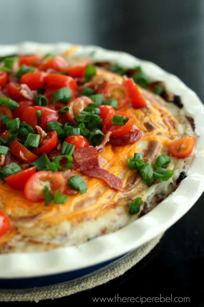 twice baked potato pie in pie plate with meat loaf crust topped with cheddar cheese and tomatoes