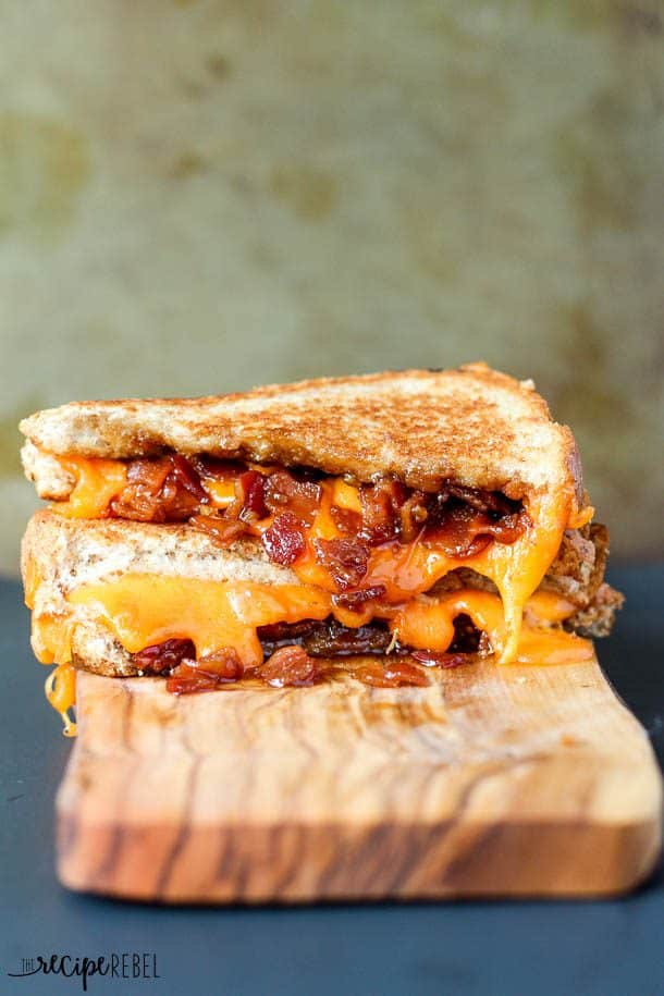 two halves of bacon jam grilled cheese stacked on wood serving board