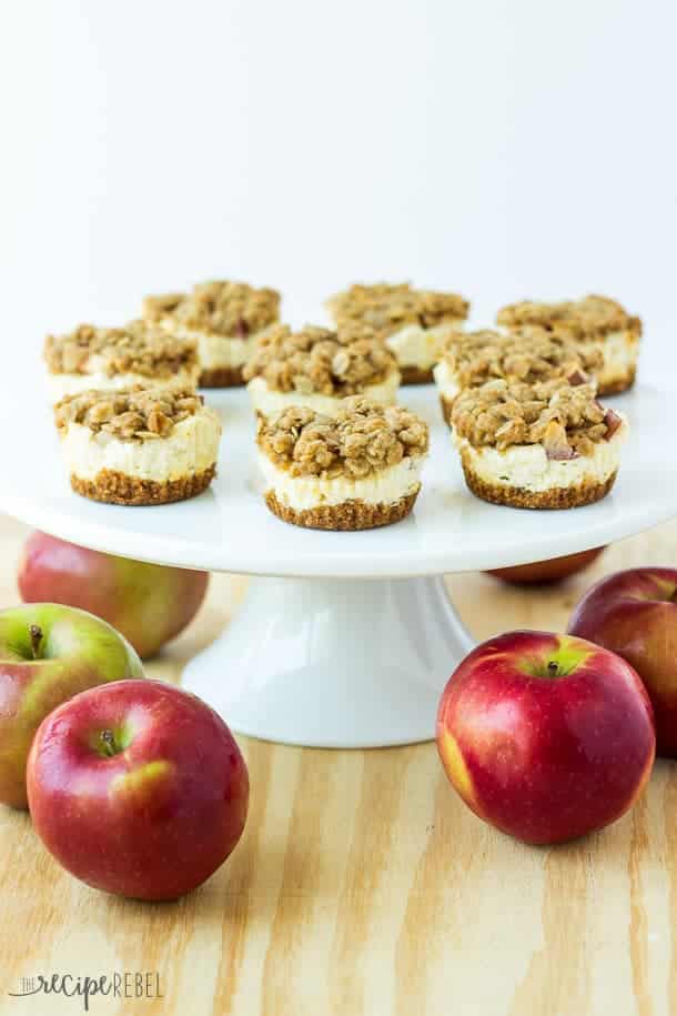 mini fruit crisp cheesecakes on white cake plate with whole apples all around