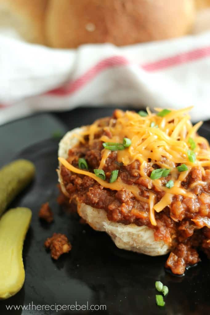 half bun on black plate with sloppy joes topped with shredded cheese and green onions