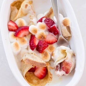 Strawberry S'more Crepe Enchiladas: Easy crepes filled with fresh strawberries, chocolate, and marshmallows, all rolled up and baked in a pan like enchiladas! Topped with vanilla custard sauce and toasted marshmallows, it's the perfect make ahead breakfast or dessert! www.thereciperebel.com