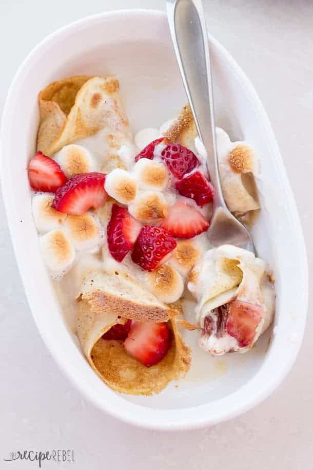 overhead image of strawberry smore crepe enchiladas in white baking dish with fork taking a bite