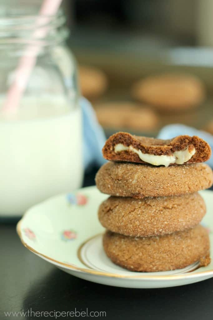 stacked of gingersnap cookies on white plate with top cookie open to reveal white chocolate filling