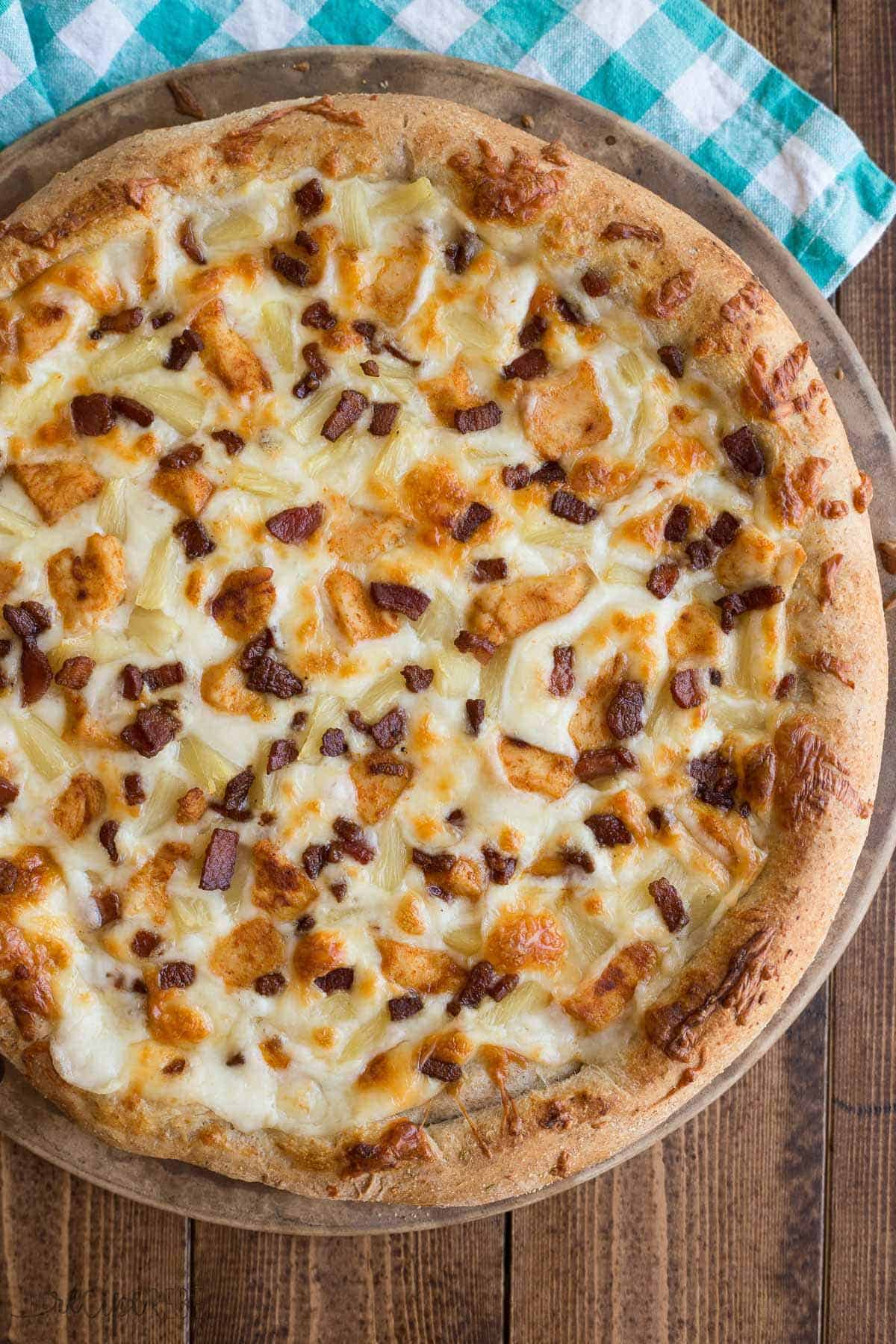 whole tropical chicken pizza on wood background with crispy bacon on top