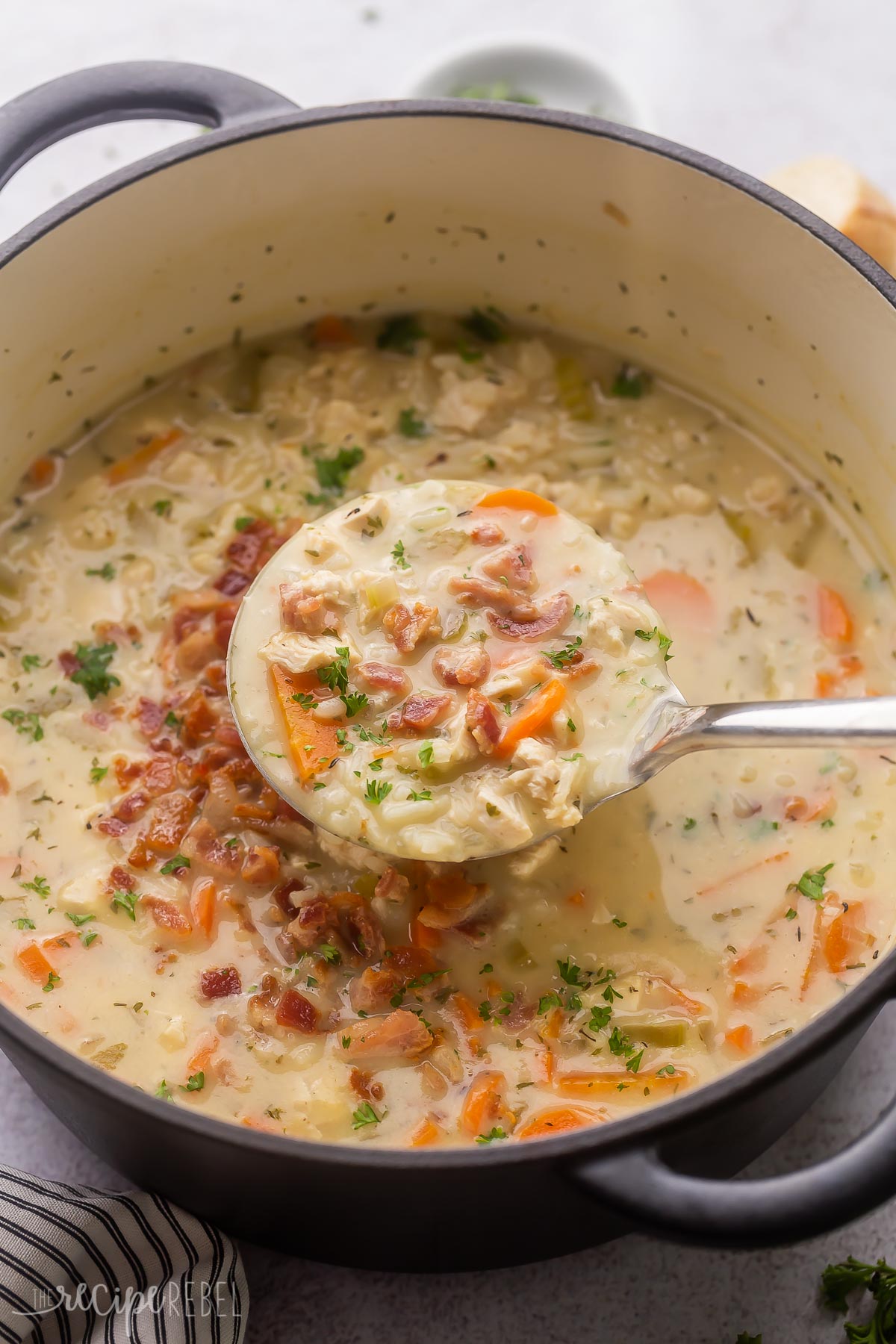 metal ladle scooping chicken bacon rice soup from pot.