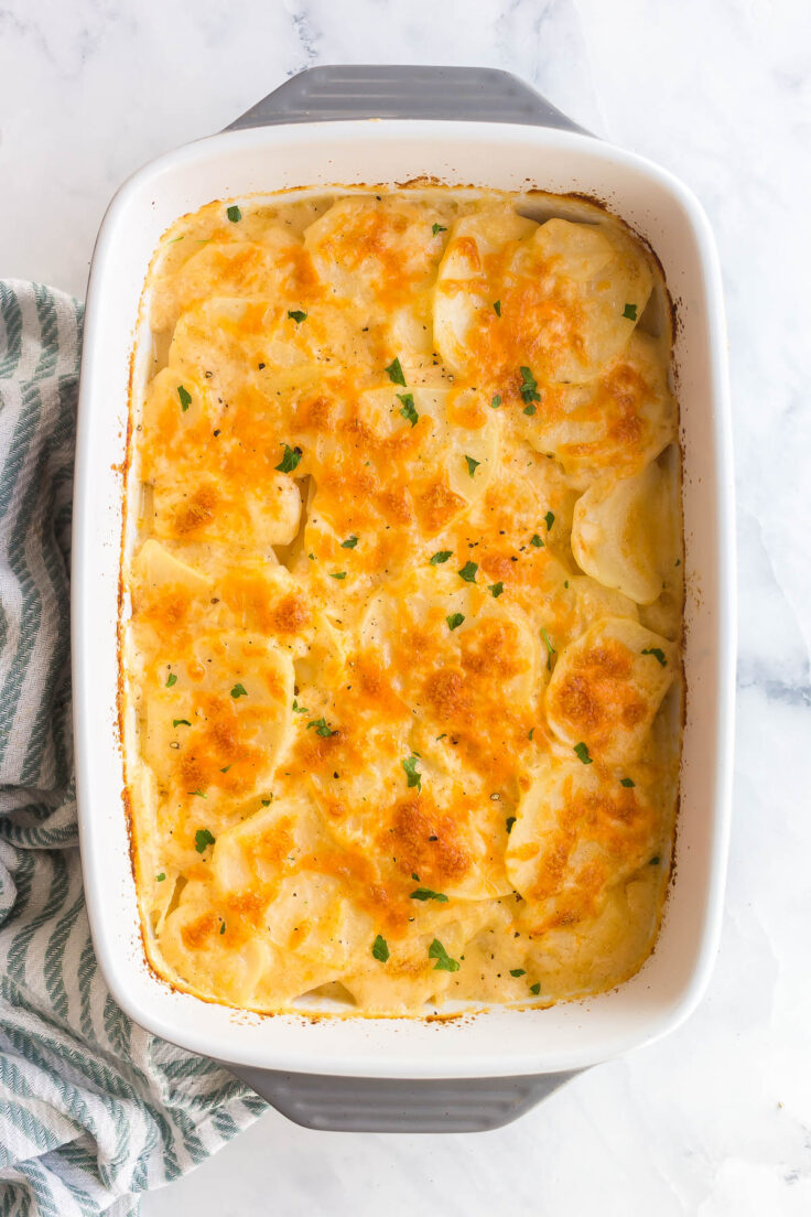 These Nacho Cheese Scalloped Potatoes are made with a spiced cream sauce, thinly sliced potatoes, and lots of cheddar cheese! overhead image of nacho cheese scalloped potatoes in grey baking dish