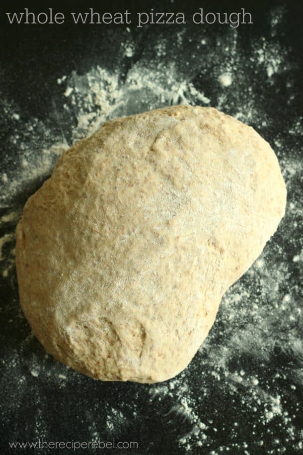 whole wheat pizza dough on black background with flour around