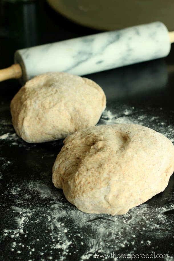two balls of whole wheat pizza dough on black table with rolling pin