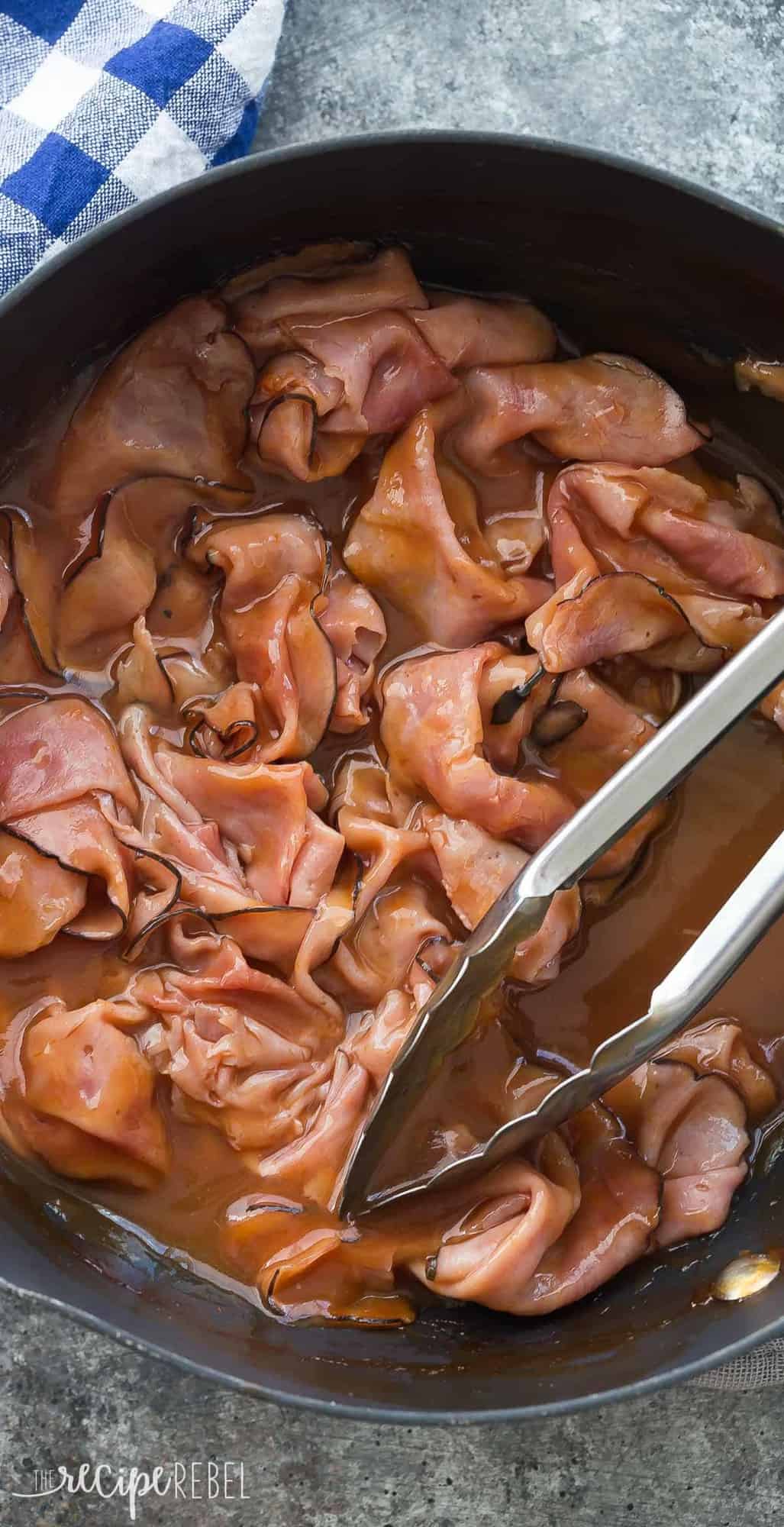 ham in barbecue sauce in large skillet with metal tongs ready to serve