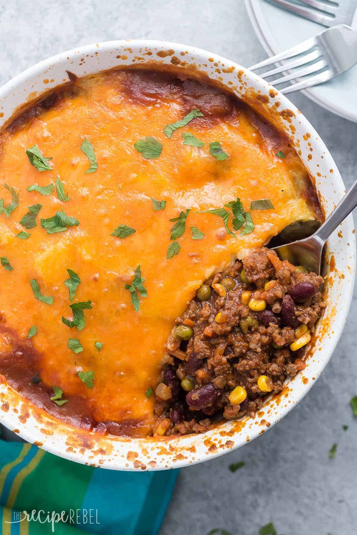 This BBQ Chili Shepherd's Pie is a fun twist on an old favorite! Classic chili with peas and carrots is topped with creamy mashed potatoes and cheddar cheese -- it's easy to make ahead! | easy dinner | easy recipe | beef | cheese | meal prep overhead image of bbq chili shepherd's pie in white casserole dish