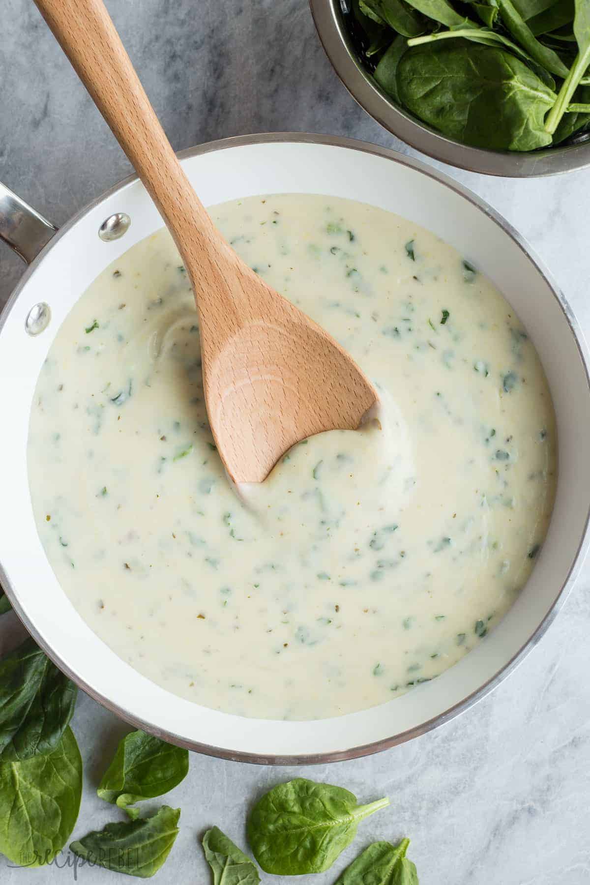 pesto spinach alfredo sauce in white skillet with wooden spoon stirring