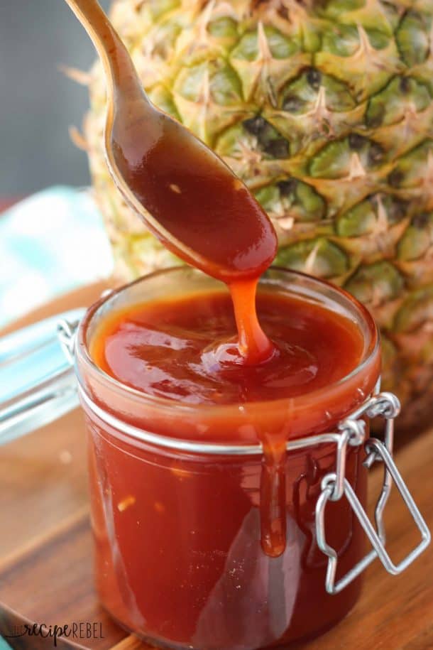 spoon scooping and drizzling barbecue sauce into jar on wooden background
