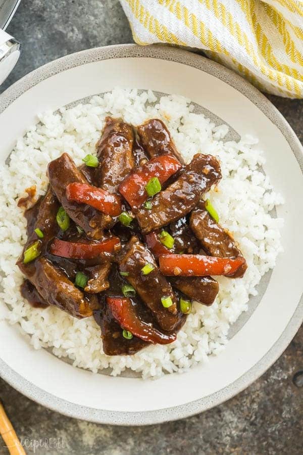 This Slow Cooker Mongolian Beef is so quick and easy -- throw everything in the crockpot and let it cook! Tender strips of steak, covered in a rich, dark sauce full of Asian flavours with a touch of sweetness. #slowcooker #crockpot #beef #mongolian #aisain #chinese slow cooker mongolian beef strips on white rice on a grey plate overhead with yellow striped towel on the side