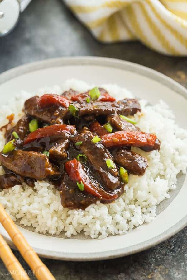 slow cooker mongolian beef on bed of white rice on a grey and white plate up close