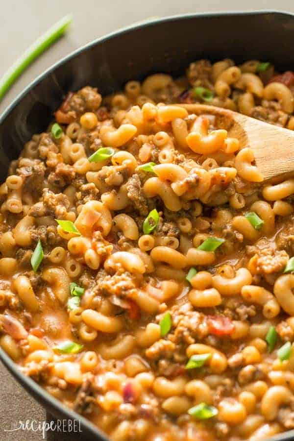 homemade hamburger helper in black skillet with green onions and wooden spoon scooping some