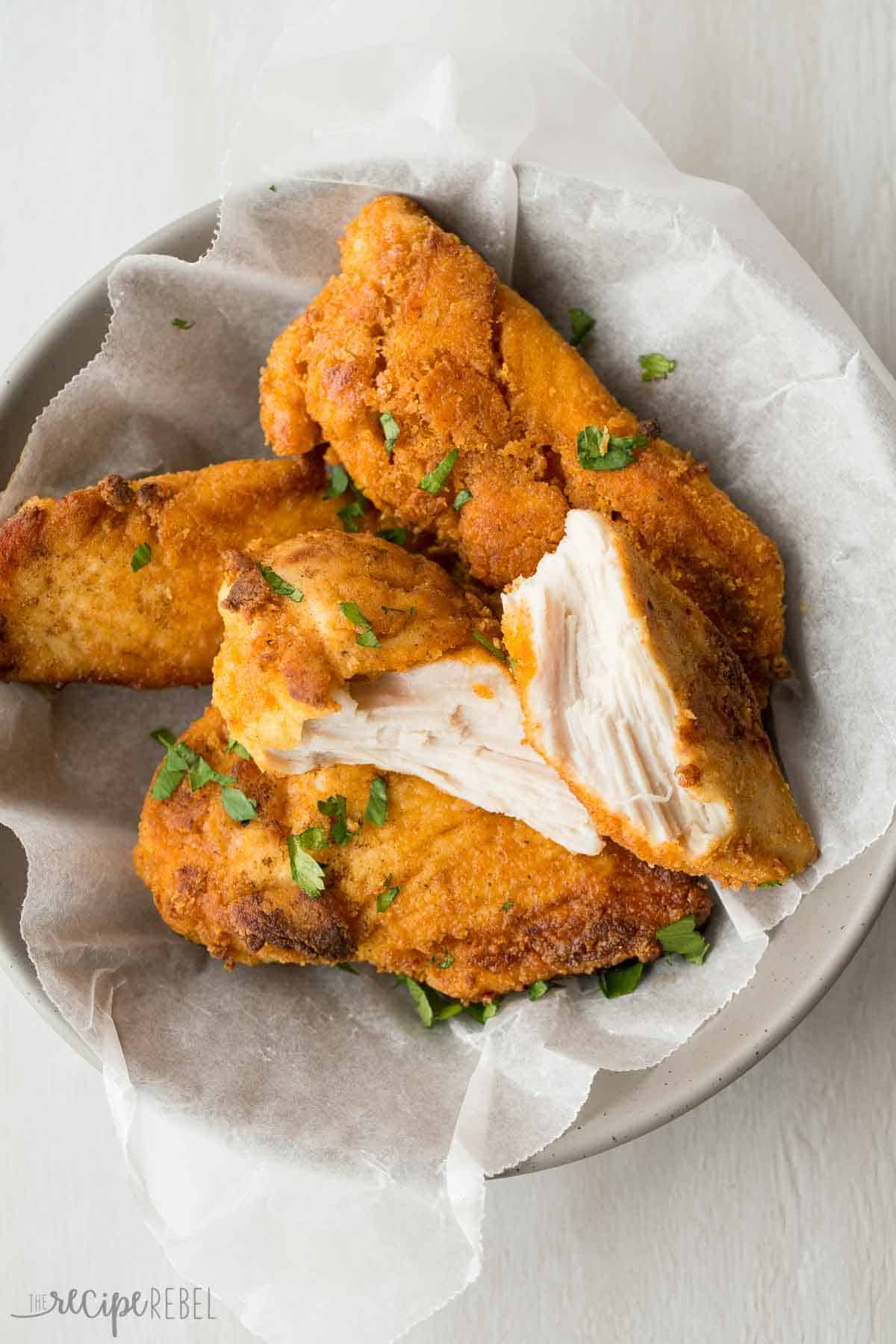 oven fried chicken pieces in grey bowl on parchment paper with one piece broken in half
