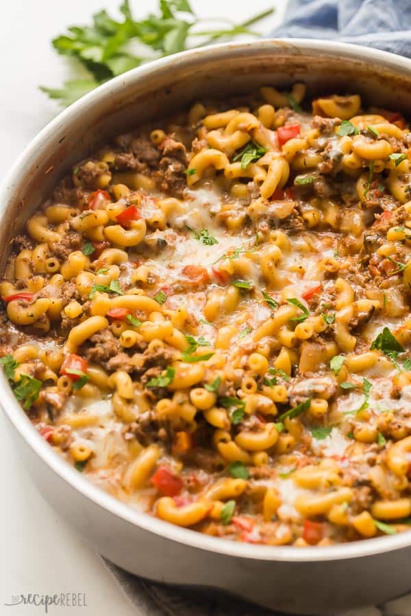 Close up image of homemade hamburger helper, with elbow pasta, cheesy sauce, ground beef, and vegetables. The dish is garnished with chopped fresh herbs.