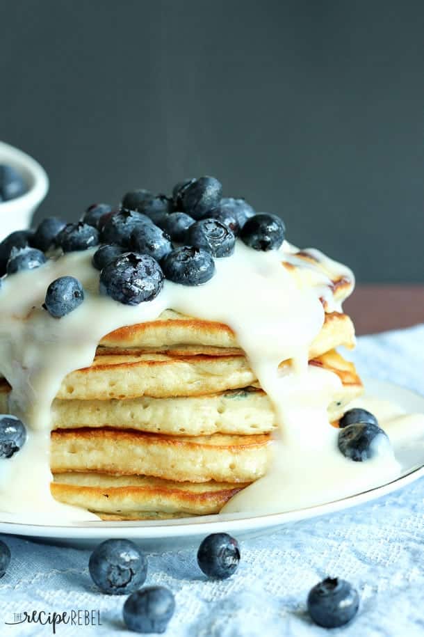stack of pancakes on white plate covered in custard sauce and fresh blueberries