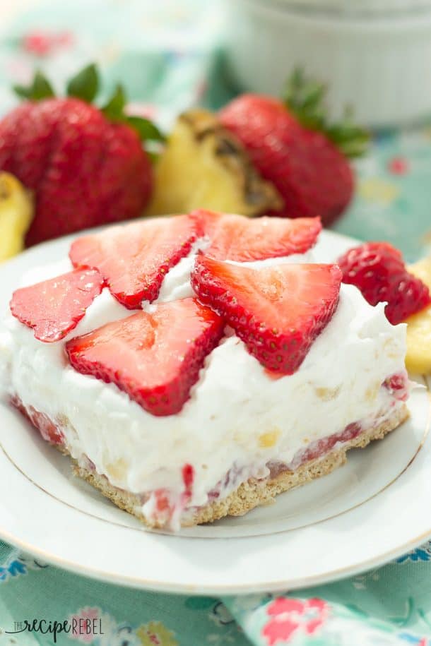 light strawberry pineapple cheesecake piece on white plate topped with strawberry slices