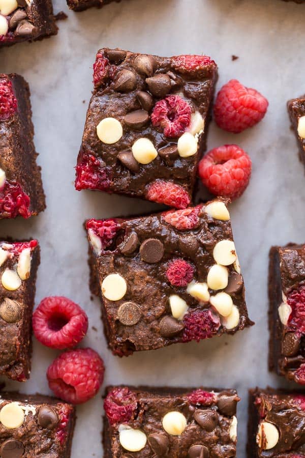 two squares of triple chocolate raspberry brownies close up with fresh raspberries