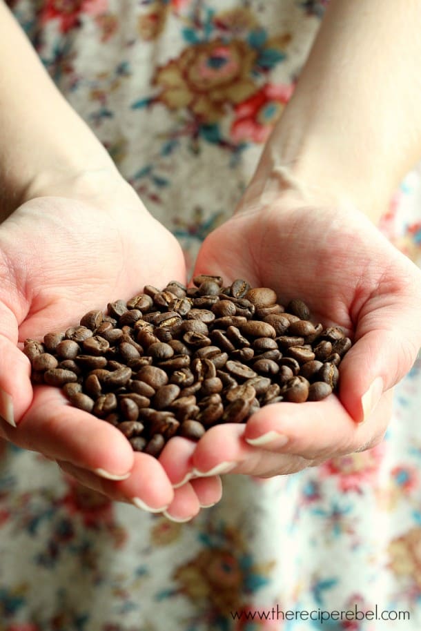 two hands holding coffee beans in front of a floral dress