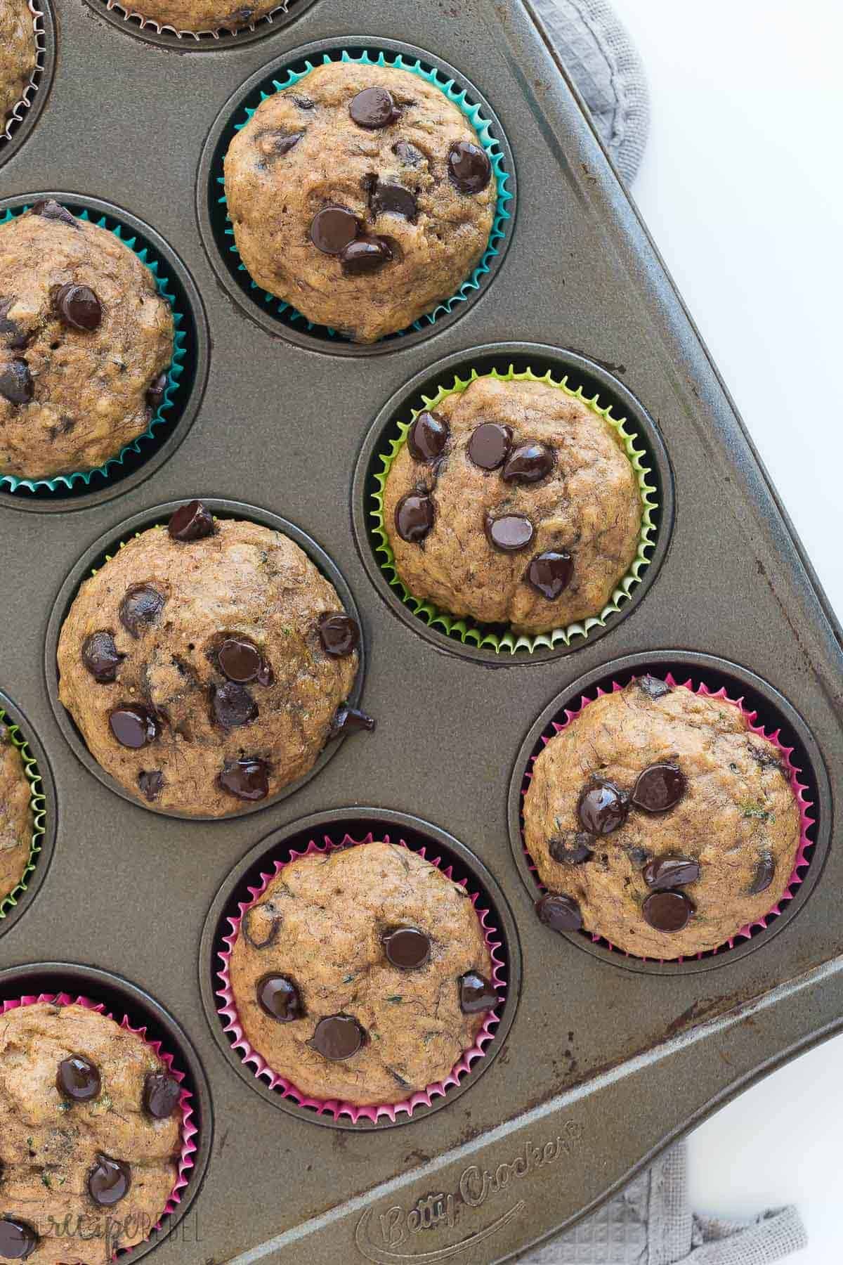 Super moist Banana Chocolate Chip Zucchini Muffins made healthier with whole wheat flour and applesauce! Perfect for that summer zucchini and a great back to school snack! Includes step by step recipe video. overhead image of muffin pan with banana chocolate chip zucchini muffins in it
