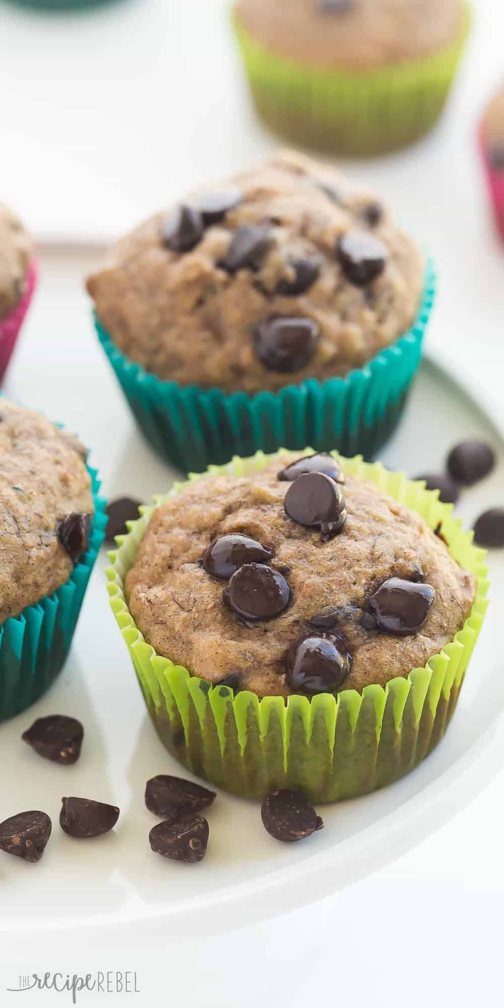 Super moist Banana Chocolate Chip Zucchini Muffins made healthier with whole wheat flour and applesauce! Perfect for that summer zucchini and a great back to school snack! Includes step by step recipe video. long photo of banana chocolate chip zucchini muffins up close on white plate