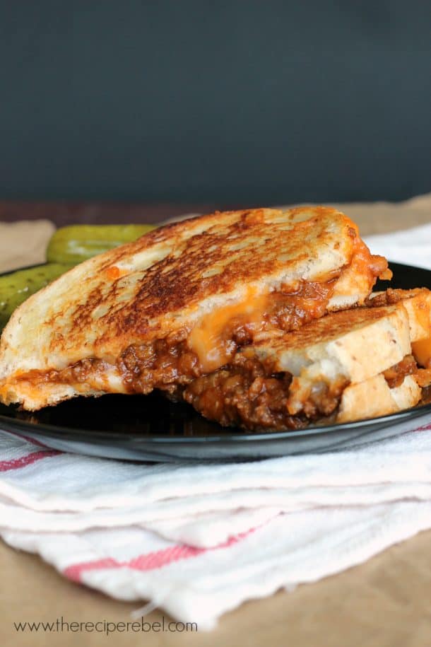 sloppy joe grilled cheese stacked on black plate with pickles on the side