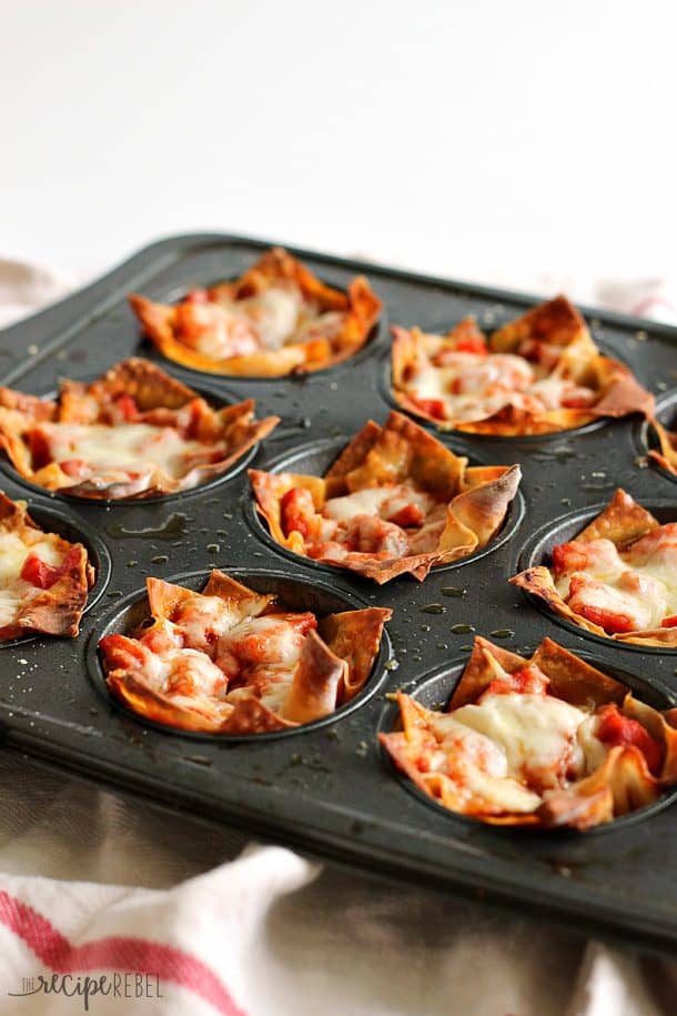 Pepperoni Pizza Cupcakes: pepperoni, cheese, and pizza sauce baked inside of crisp wonton wrappers: the ultimate handheld pizza! Only 4 main ingredients and 20 minutes! Perfect as an appetizer or a quick lunch. www.thereciperebel.com pepperoni pizza cupcakes in non stick muffin pan on white background