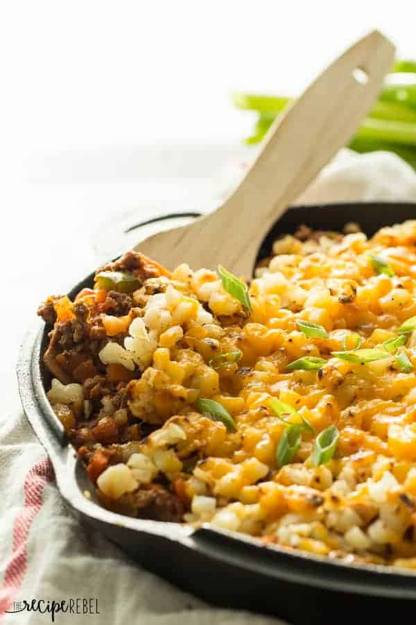 wooden spoon scooping taco beef and hashbrown skillet topped with cheese