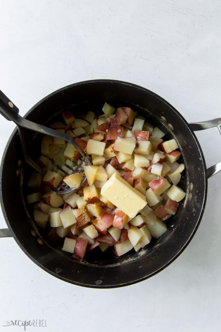 cooked potatoes in pot being mashed with butter