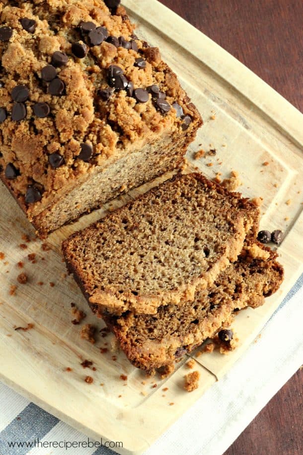 banana bread with streusel and chocolate chips on wood cutting board with two slices cut