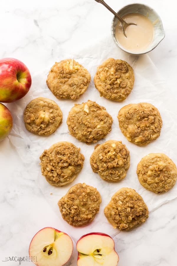 A scratch-made cookie filled with fresh apple chunks and topped with brown sugar cinnamon streusel, drizzle with maple glaze. All the flavors of apple crisp in a chewy cookie! #apple #cookies #baking #dessert overhead image of apple crisp cookies on white background