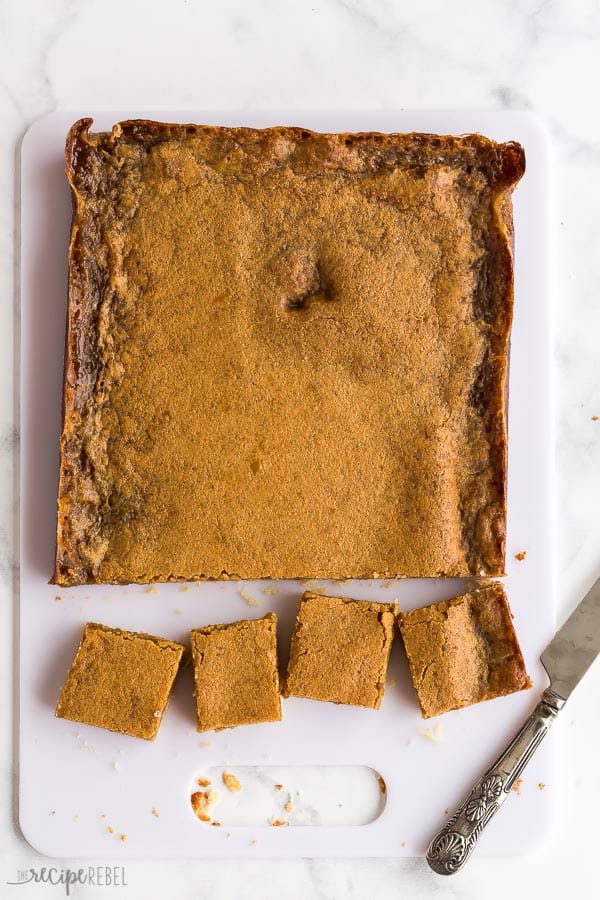 These Butter Tart Squares are so sweet and gooey -- a shortbread crust makes these so easy and SO good! So much quicker than butter tarts. #baking #dessert #recipes #Christmas butter tart squares overhead whole with four pieces cut on white cutting board