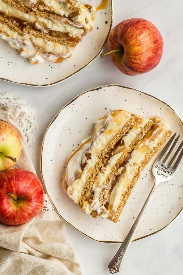 two slices of apple icebox cake on two white plates with whole apples