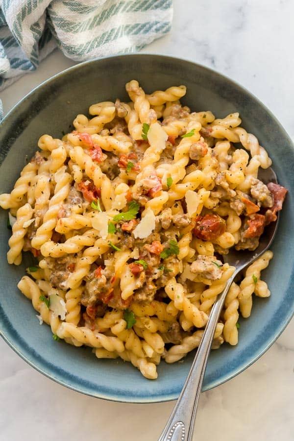 tomato pesto pasta in blue bowl with fork stuck in noodles