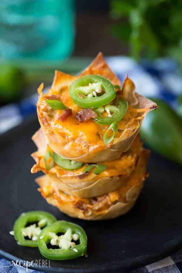 stack of three jalapeno popper wonton cups on black plate topped with jalapeno slices