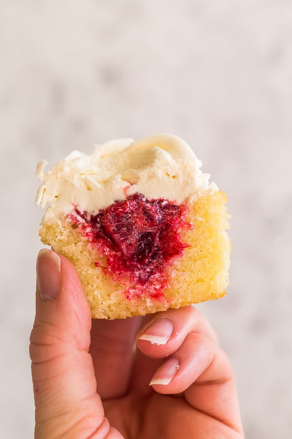 hand holding up cranberry cupcake revealing filling