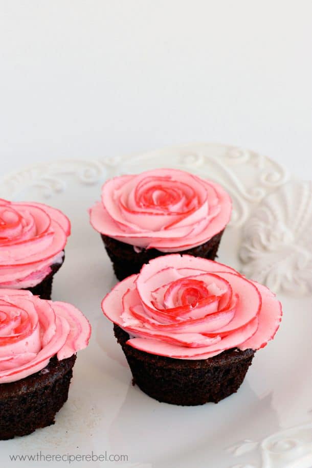 four chocolate cupcakes with pink buttercream roses on white platter