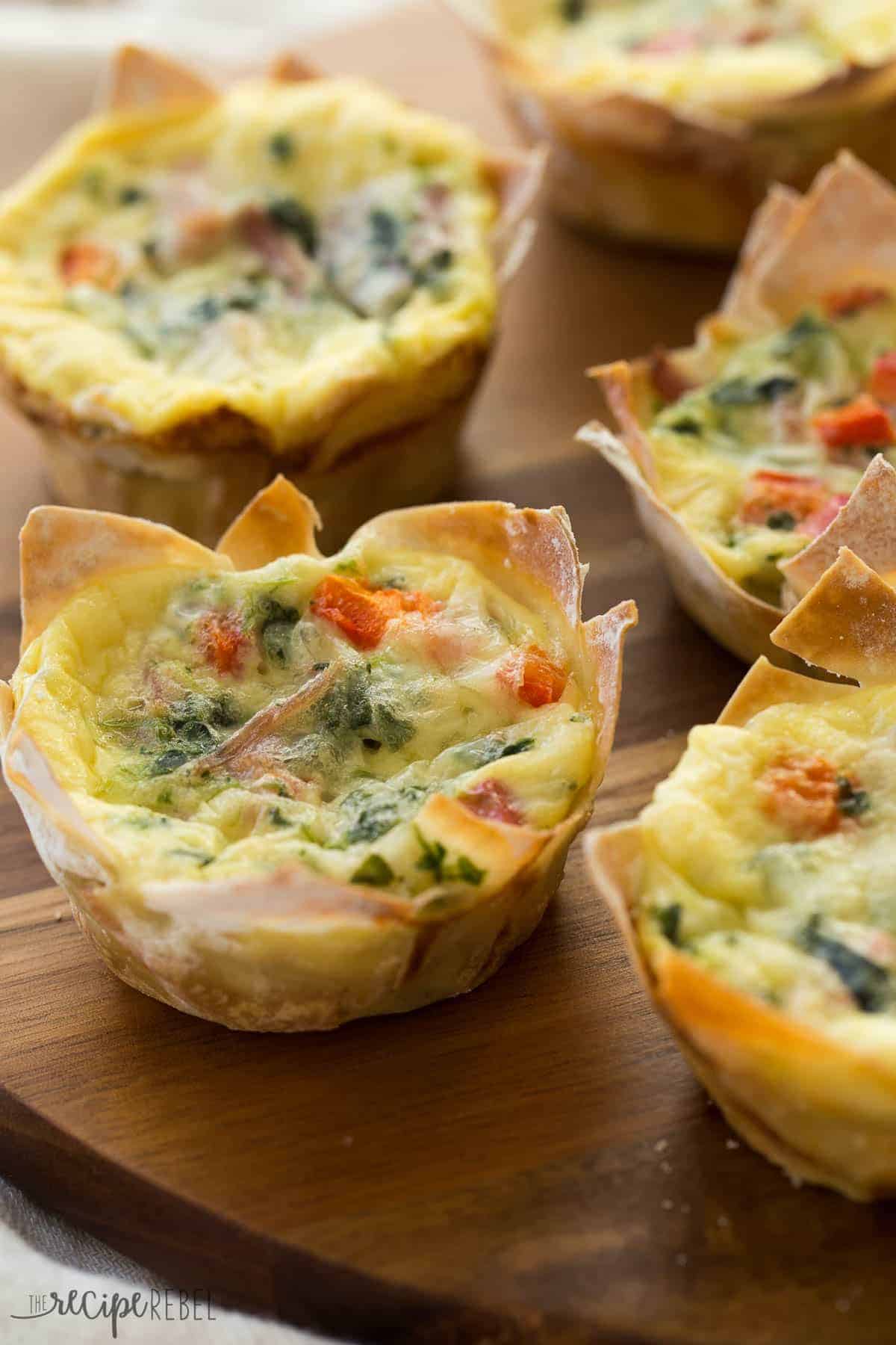 Wonton wrappers make these mini wonton quiche so quick and easy! The perfect appetizer for holidays, brunch, or brinner! mini quiche in wonton wrappers on a wooden board