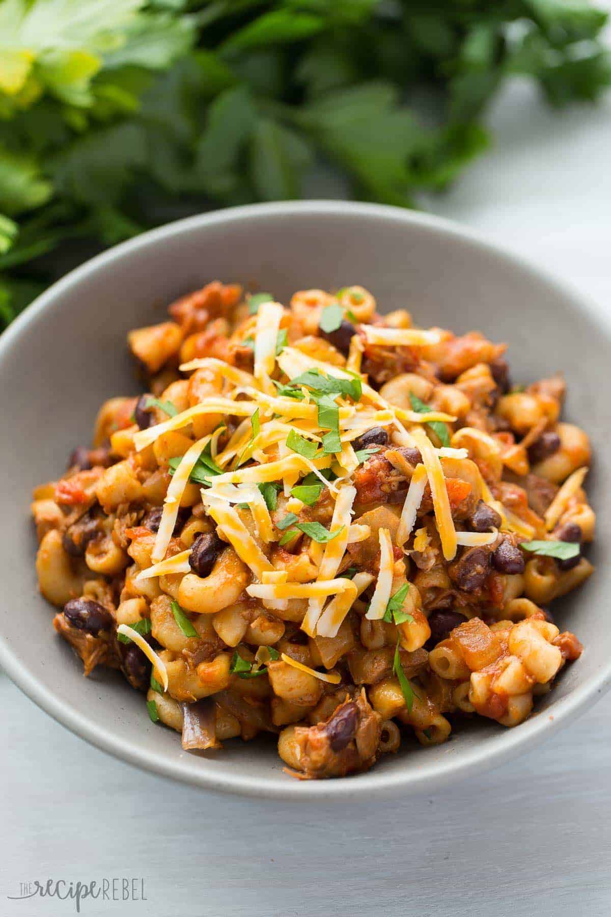 slow cooker bbq chili mac in grey bowl topped with shredded cheese and parsley