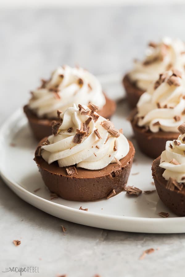 mini chocolate cheesecakes on white plate with whipped cream and chocolate shavings