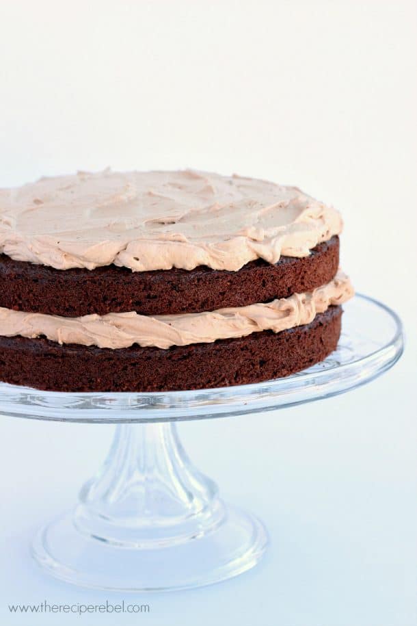 two layer gluten free chocolate cake on clear cake plate on white background