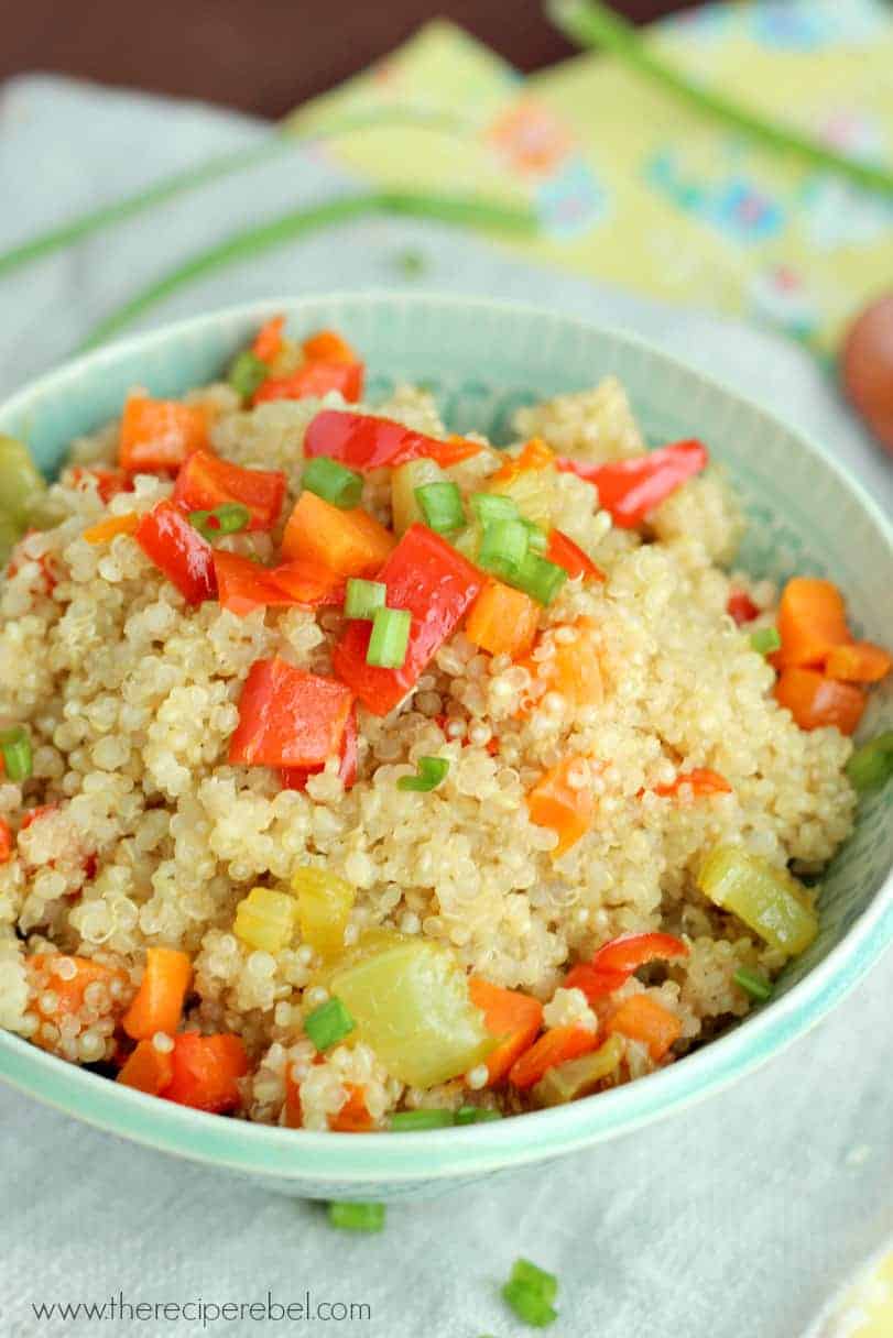 blue bowl filled with quinoa pilaf topped with red peppers carrots and green onions