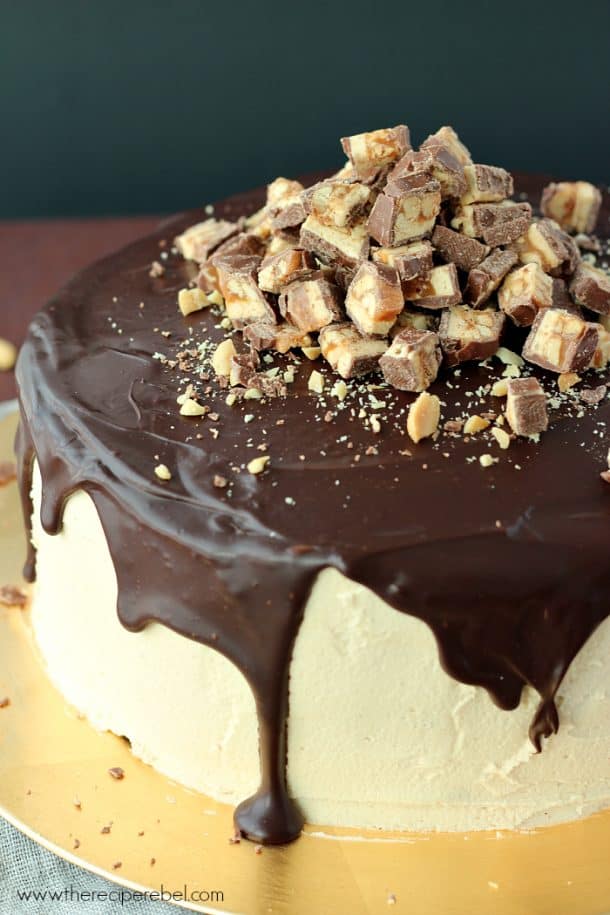 close up of whole snickers cheesecake cake with peanut butter frosting and chocolate ganache
