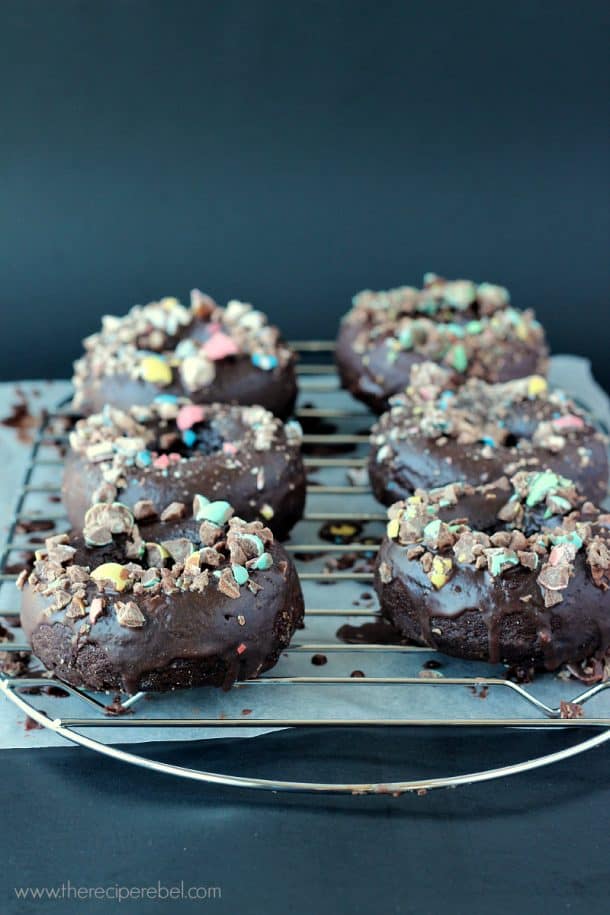 six double chocolate baked donuts lined up on a wire cooling rack over parchment