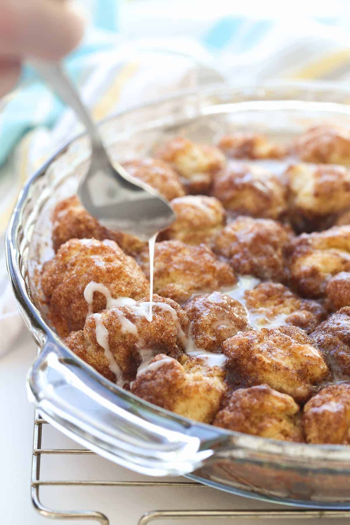 cinnamon roll bites in glass pie plate with spoon drizzling glaze