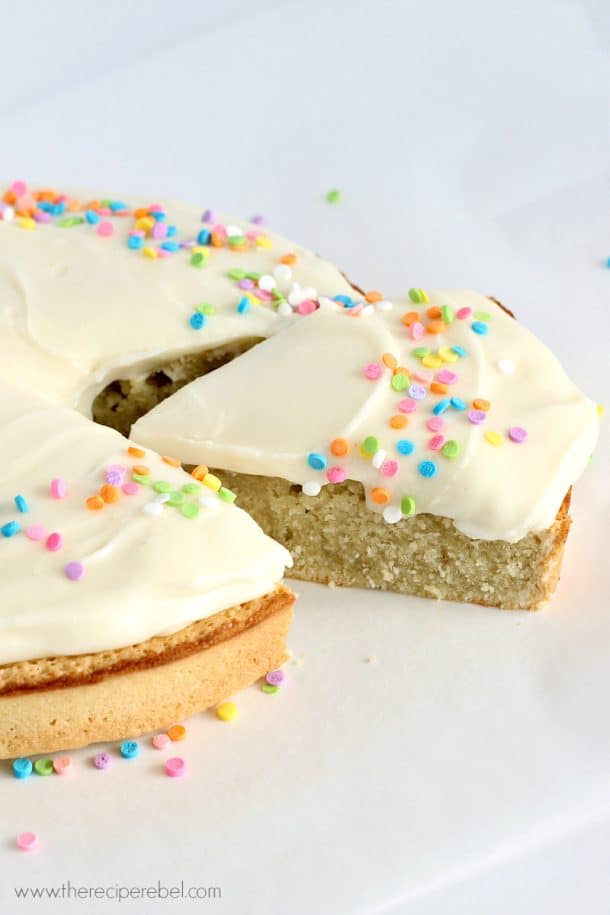 one layer gluten free coconut cake on parchment paper topped with cream cheese frosting and sprinkles